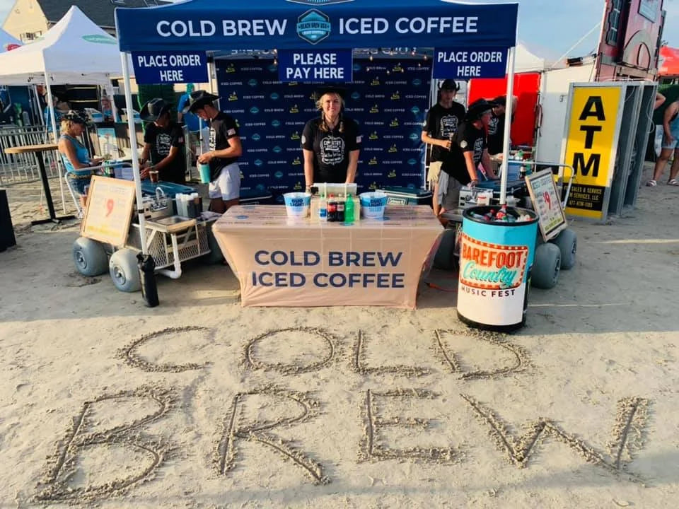 Cold brew iced coffee stand on a beach with 'Cold Brew' written in sand. At Barefoot Country Music Fest.