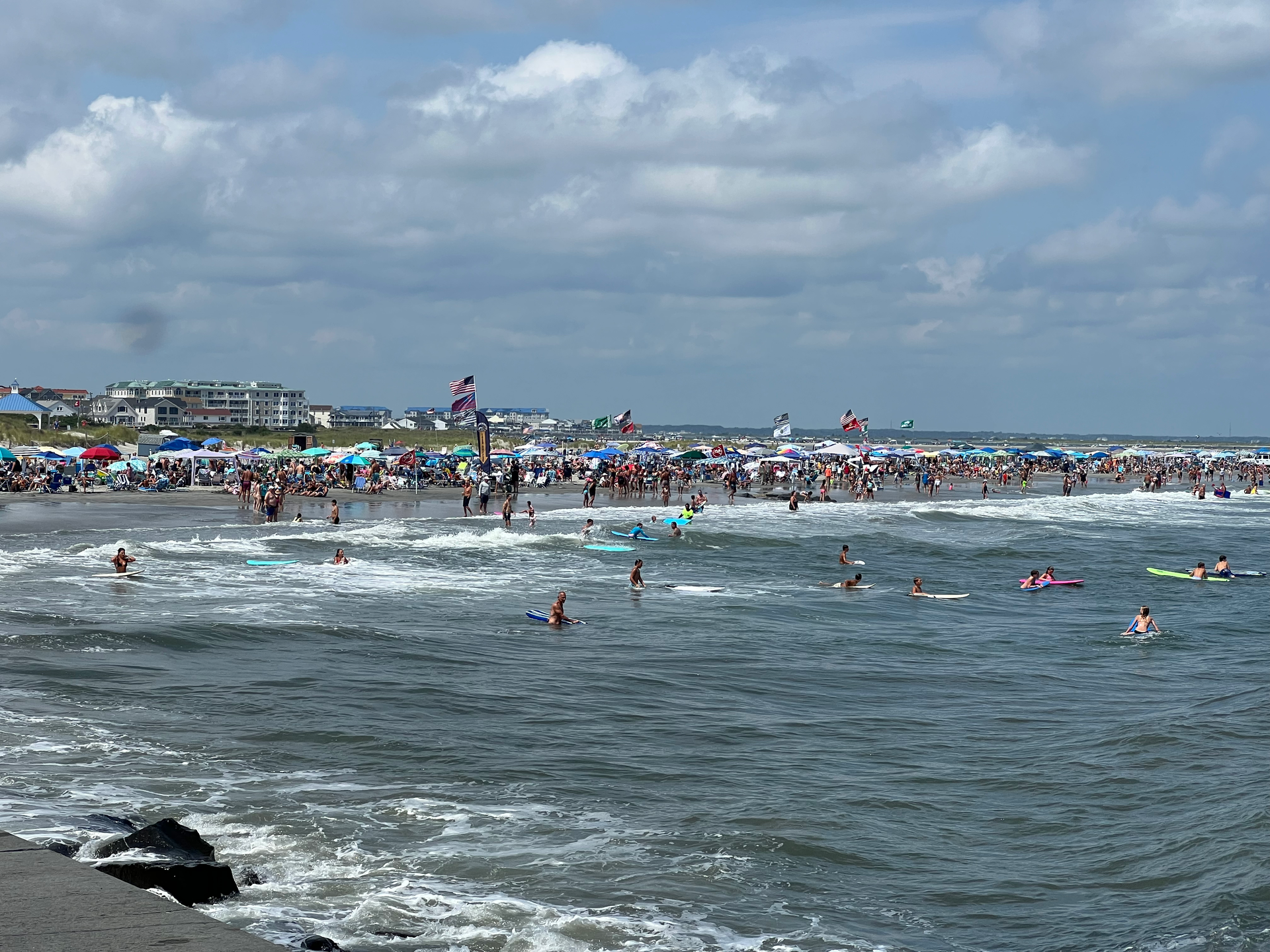 Beach scene with people in the water and a cloudy sky.